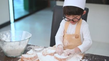 Gözlük, şef şapka ve önlük oynayan ve ev mutfağında fırın pişirme komik sevimli küçük Asyalı çocuk. Ev yapımı yemekler ve ekmek. Eğitim ve öğrenme kavramı. Portre ve rüya iş meslek.