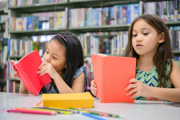 Две маленькие милые девочки многонациональные друзья читают книги вместе — стоковое фото