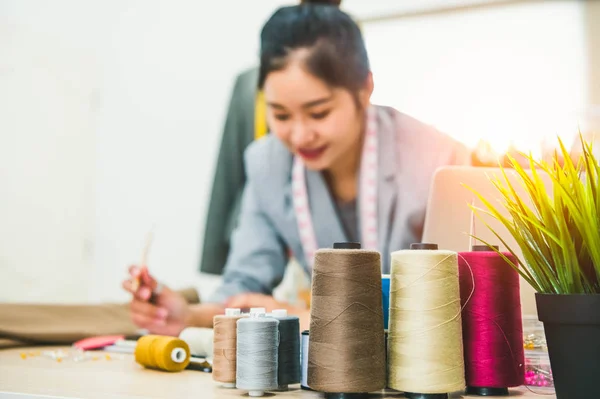 Closeup of color thread with blurry happy female tailor and sewi