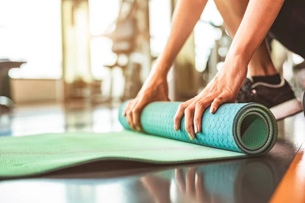 Close up of sporty woman folding yoga mattress in sport fitness
