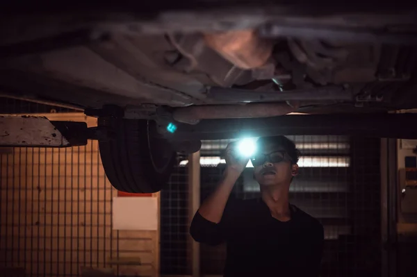 Lonely Asian male shining flashlight to examine car under chassi — Stock Photo, Image