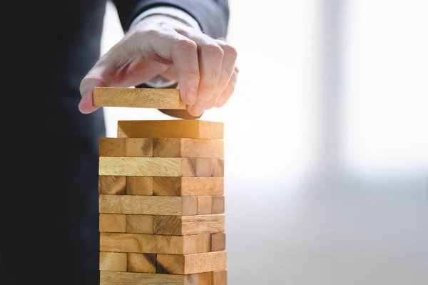 Businessman arranging wood block and stacking as tower by hand. — Stock Photo, Image