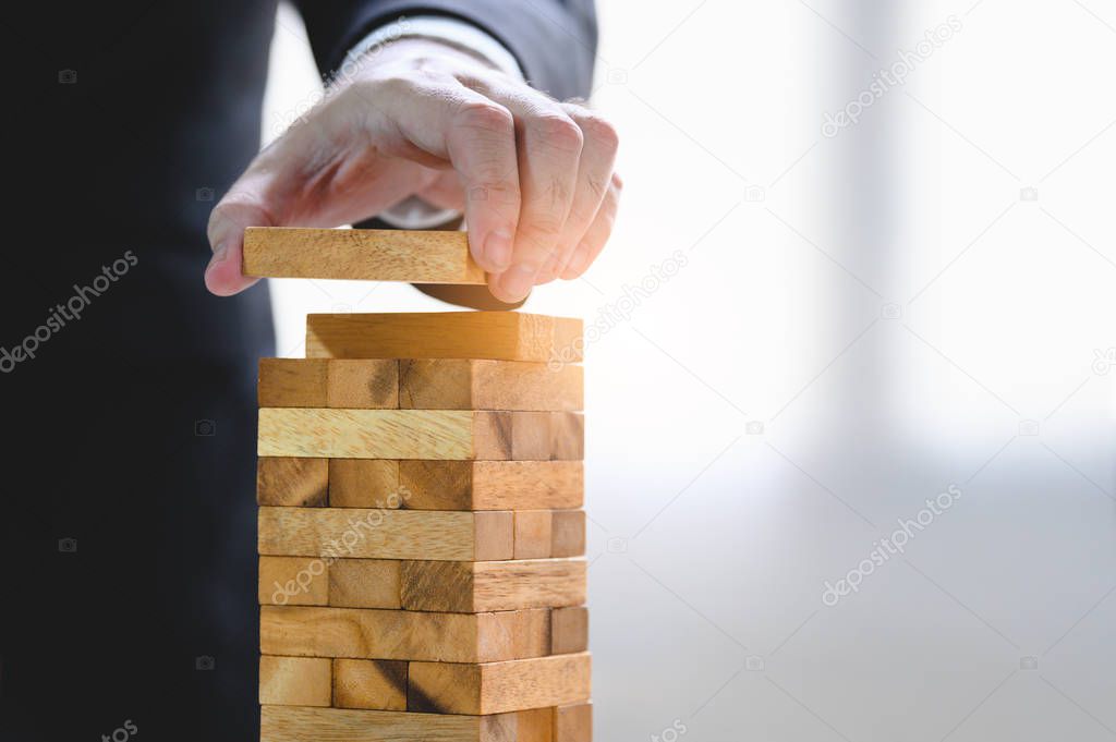 Businessman arranging wood block and stacking as tower by hand. 