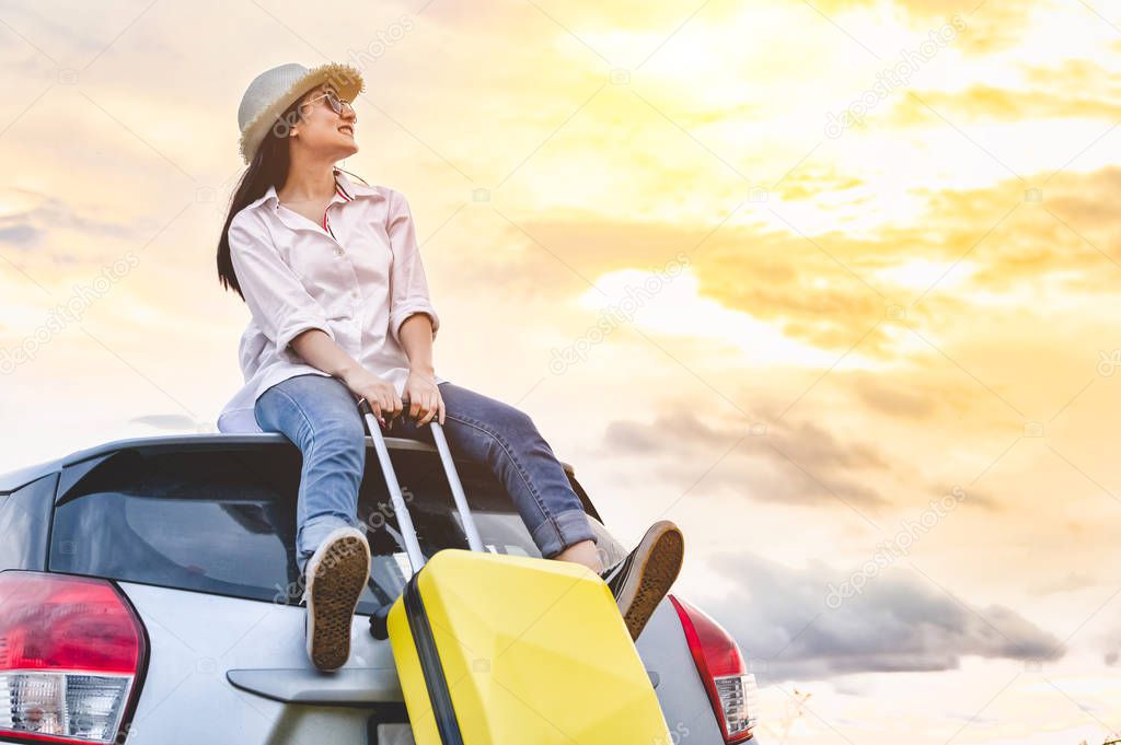 Happy Asian woman on top of car with luggage bag. Girl sitting o