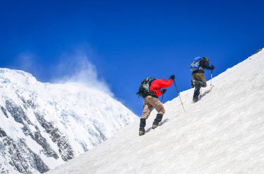 Kar yağdı doruklarına arka plan, Himalayalar ile sarp bir tepe üzerinde yürüyen iki dağ backpackers