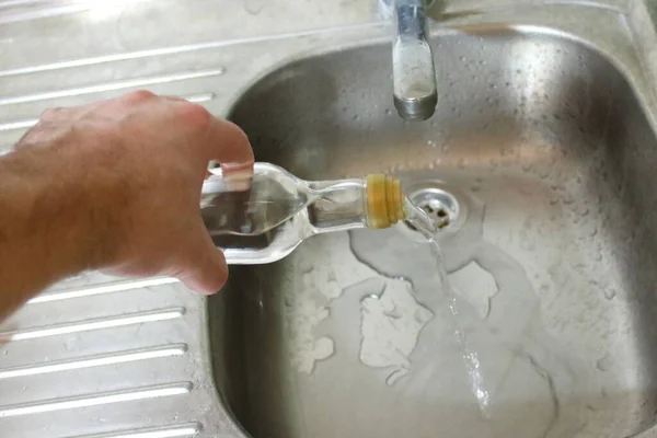 Pouring alcohol into the sink in the kitchen. No to alcohol. Stop the alcohol. Healthy lifestyle. A man pours alcohol from a bottle into the kitchen sink.