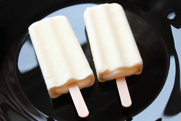 Creamy ice cream on a stick in white glaze on a black plate.