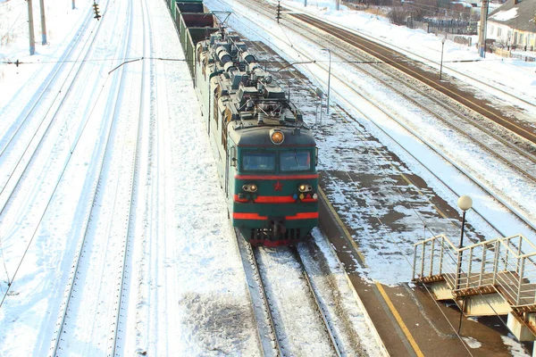 Cargo trunk two-section electric locomotive of alternating current 25 kV with axial formula. A train with empty cars passing through a railway station. Russia.