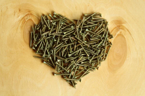 Heart made of silver screws on plywood. Close-up. Background.