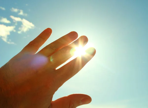 The man\'s hand covers the sun. The man closes the palm of sunlight. Close-up. Background.