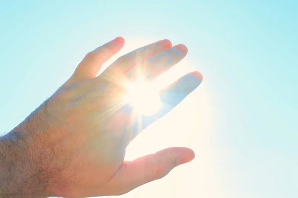 Male hand covers the sun. The sun\'s rays shine through the hand. Close-up. Background. Texture.