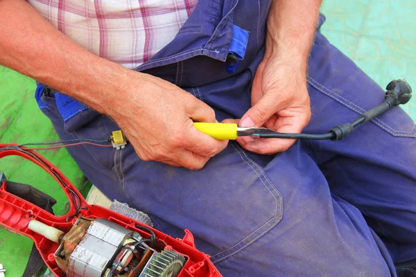 A man repairs an electric lawn mower. Trimmer. Background.