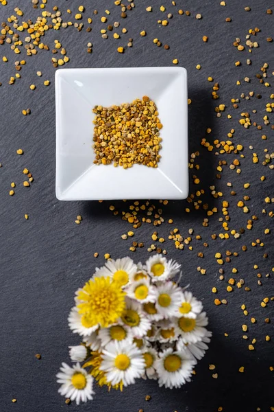 small bowl of pollen grains with small bunch of flowers out of f