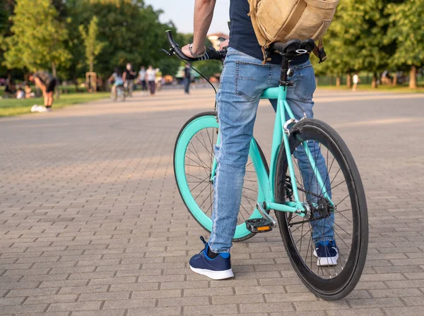 minimal bike in the foreground, ridden by a man with a backpack on his shoulders, symbol of freedom and movement in the city, background of green city area