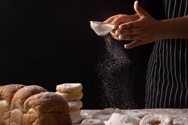 Şef hazırlanıyor ekmek hamur ve krema şeker siyah arka plan üzerinde gıda kavramı izole ahşap tablo ile çörek yağmurlama eller.