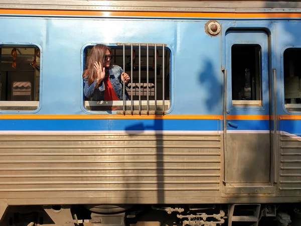 美丽的亚洲女人戴着太阳镜从窗户往外看 从离港列车上挥手告别的肖像 免版税图库图片