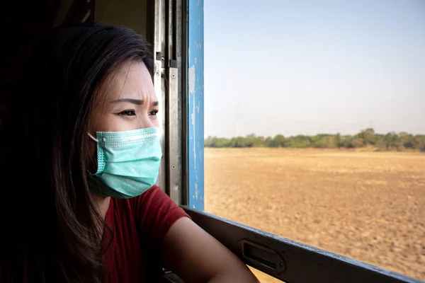 列車の窓の近くに座って 電車の窓を通して見る空気汚染のためフェイス マスクを着た若いアジア女性の肖像画 ストック写真