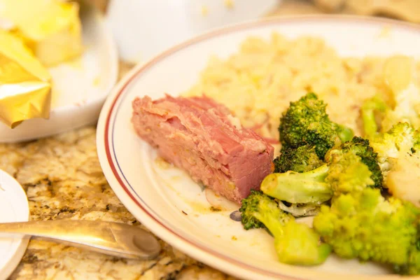 Ceramic plate with corned beef, broccoli, and rice in a kitchen setting.