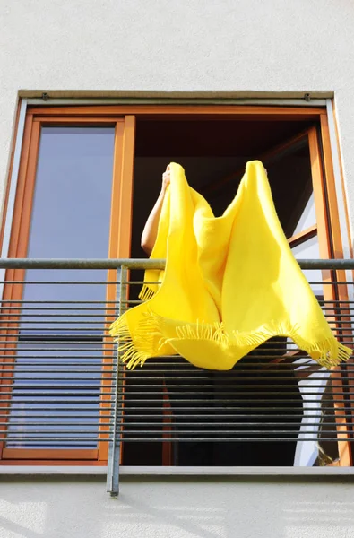 woman shaking out a yellow blanket with vibrant color from a window, low angle view