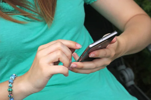 bir akıllı telefon kullanan genç kadın uzun saçlı ve bir şezlong içinde oturan bir yeşil gömlek