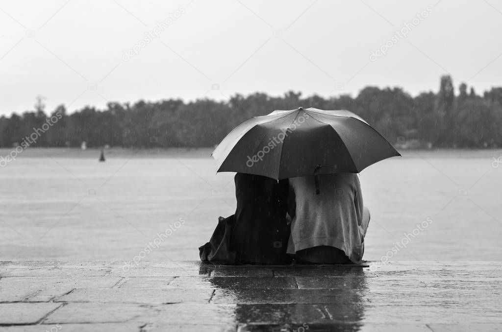 couple lovers sitting under umbrella in rainy weather