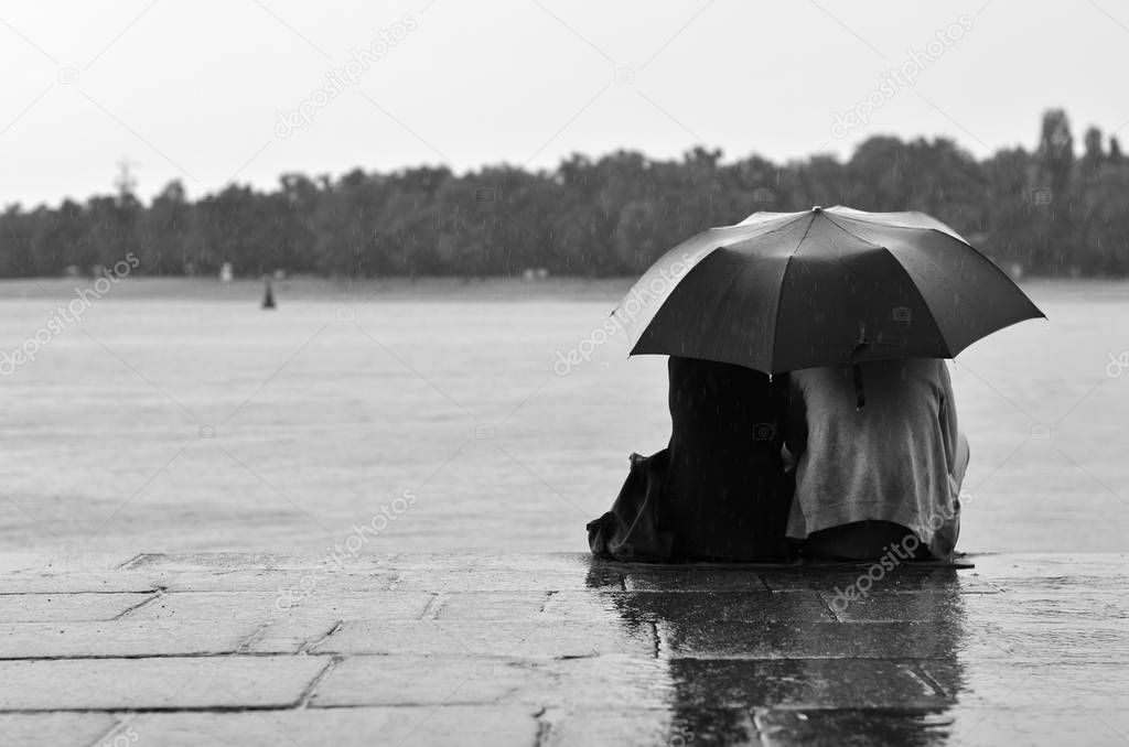 lovers couple sitting on quay in rain
