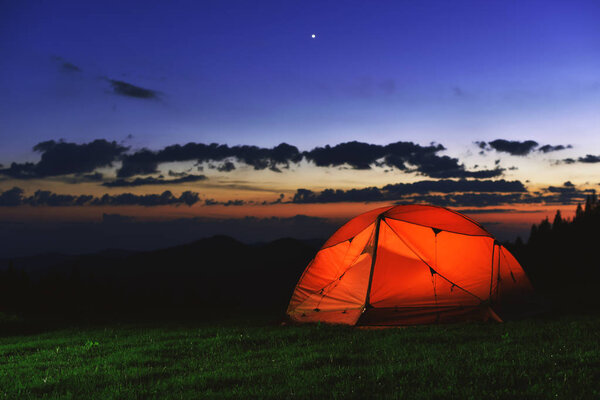 orange tourist tent stand on grass in spring night mountains