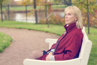 Parkta bir bankta oturan düşünceli üst düzey kadın