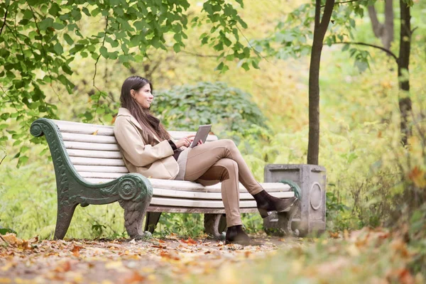 使用数字平板电脑 坐在秋天公园的女人 — 图库照片