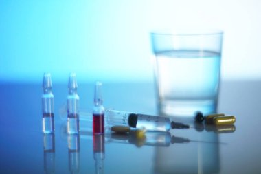 Şırınga, ampul ve haplar parlak mavi canlandırma ışığı arka planında