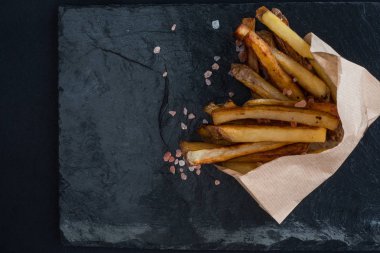 Kağıt bardakta patates kızartması ve siyah taştan bir arka planda Himalaya pembe tuzu. Lüks restoran konsepti.