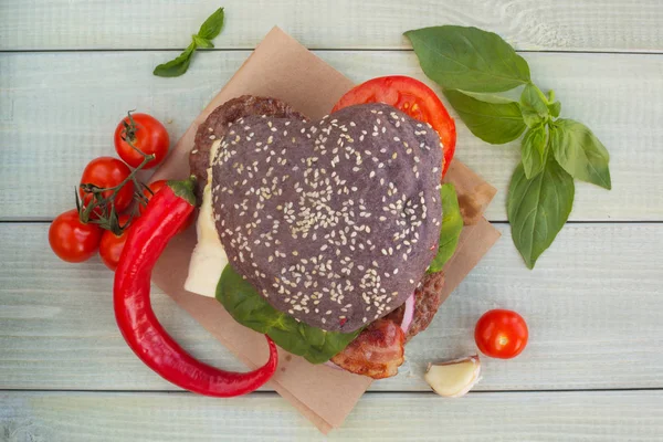 Heart shaped black hamburger and ingredients on wooden background, love burger fast food concept, Valentines day surprise dinner, wooden background, top view flat lay