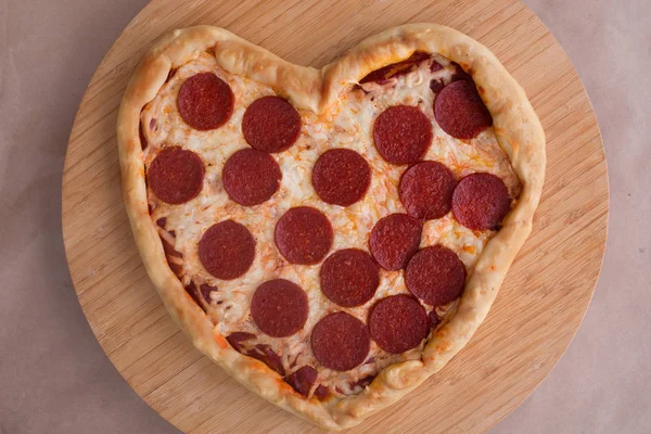 Pizza heart shaped with pepperoni on wooden background. Concept of romantic love for Valentines Day . Love food