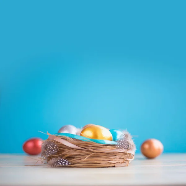 美しいハッピーイースターの休日の挨拶バナーとともにイースターの巣色の卵と青のテキストのためのコピースペースと光木製の背景にリボンで飾られています — ストック写真
