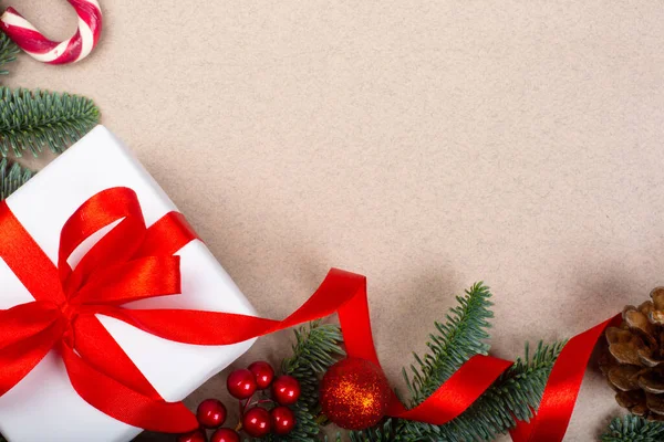 伝統的な緑のクリスマスの贈り物白い箱の中に赤いリボンの弓の木高貴なモミのコーンとホリーベリーの国境フレーム上のクラフト紙の背景コピースペーステキスト用 — ストック写真