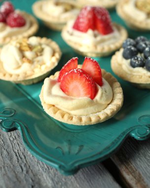 Yaban mersini, çilek ve antep fıstığı tartlets ve kaşık ahşap bir masa üzerinde