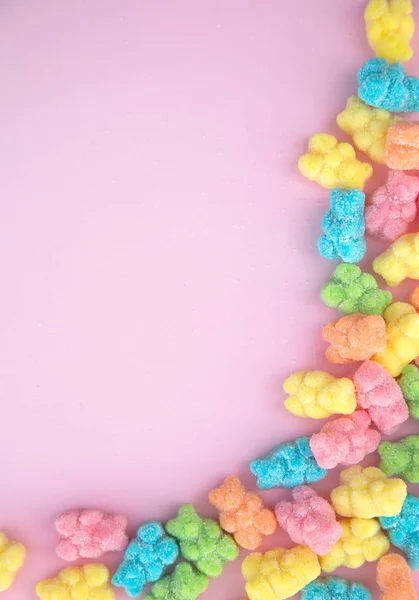 Yellow, blue, green and pink gummy bears on a pink background