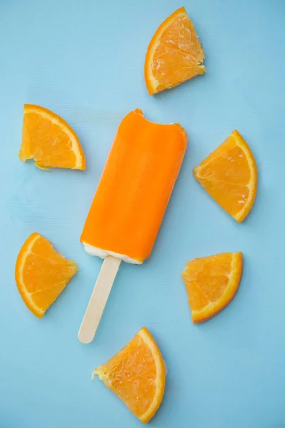 orange popsicle with few slice of orange on a blue background