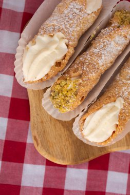 Taze cannoli doğasının üst görüntüsü ve kırmızı kareli masa örtüsünün üzerindeki kesme tahtasındaki fıstıklı kağıt üzerinde