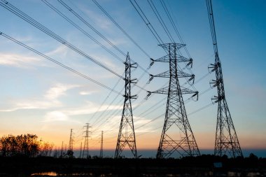 Gökyüzü günbatımı arka planında yüksek voltaj direği.