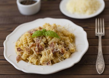 Ev yapımı makarna carbonara İtalyanca ile pastırma, yumurta, karanlık bir arka plan üzerinde beyaz tabakta Parmesan peyniri.