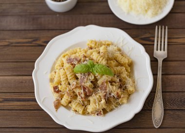 Ev yapımı makarna carbonara İtalyanca ile pastırma, yumurta, karanlık bir arka plan üzerinde beyaz tabakta Parmesan peyniri.