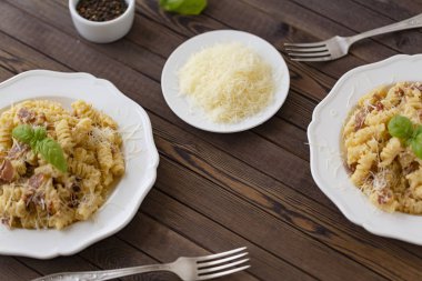 Ev yapımı makarna carbonara İtalyanca ile pastırma, yumurta, karanlık bir arka plan üzerinde beyaz tabakta Parmesan peyniri.