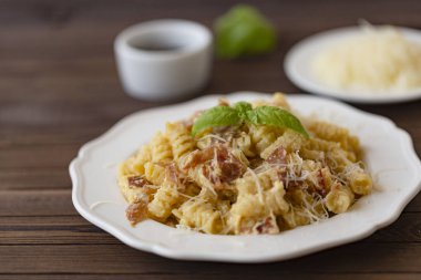 Ev yapımı makarna carbonara İtalyanca ile pastırma, yumurta, karanlık bir arka plan üzerinde beyaz tabakta Parmesan peyniri.