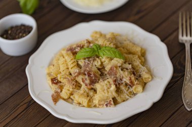 Ev yapımı makarna carbonara İtalyanca ile pastırma, yumurta, karanlık bir arka plan üzerinde beyaz tabakta Parmesan peyniri.