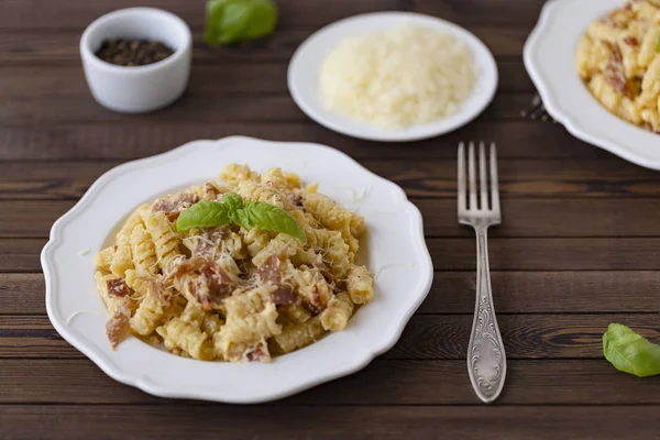 Ev yapımı makarna carbonara İtalyanca ile pastırma, yumurta, karanlık bir arka plan üzerinde beyaz tabakta Parmesan peyniri.
