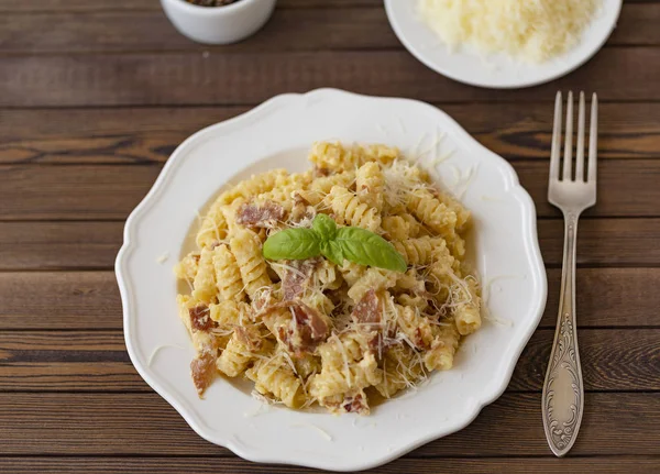 Ev yapımı makarna carbonara İtalyanca ile pastırma, yumurta, karanlık bir arka plan üzerinde beyaz tabakta Parmesan peyniri.