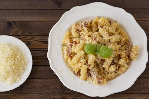 Ev yapımı makarna carbonara İtalyanca ile pastırma, yumurta, karanlık bir arka plan üzerinde beyaz tabakta Parmesan peyniri.