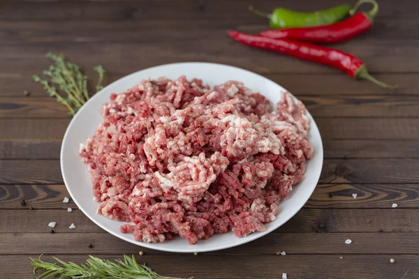 Raw ground beef and other ingredients on a wooden table, in a white plate