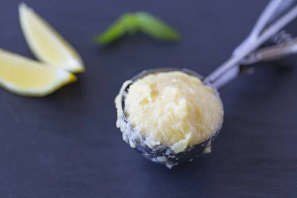 Lemon ice cream,  fruit sorbet  in a spoon for ice cream on slate background.